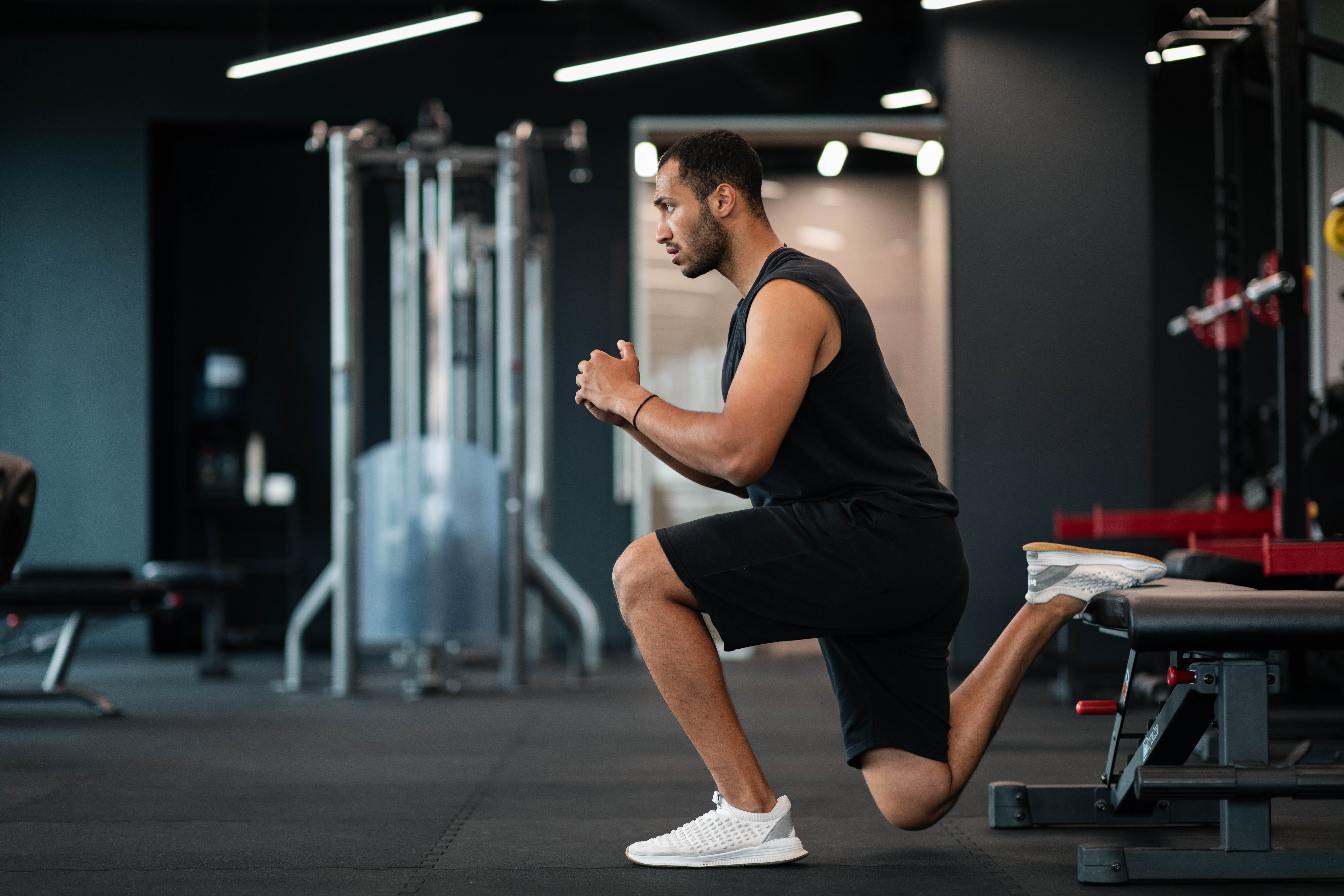 Man doing a split squat with a bench holding up one foot in the gym